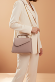 Person wearing a light-colored suit with a matching handbag against a beige background
