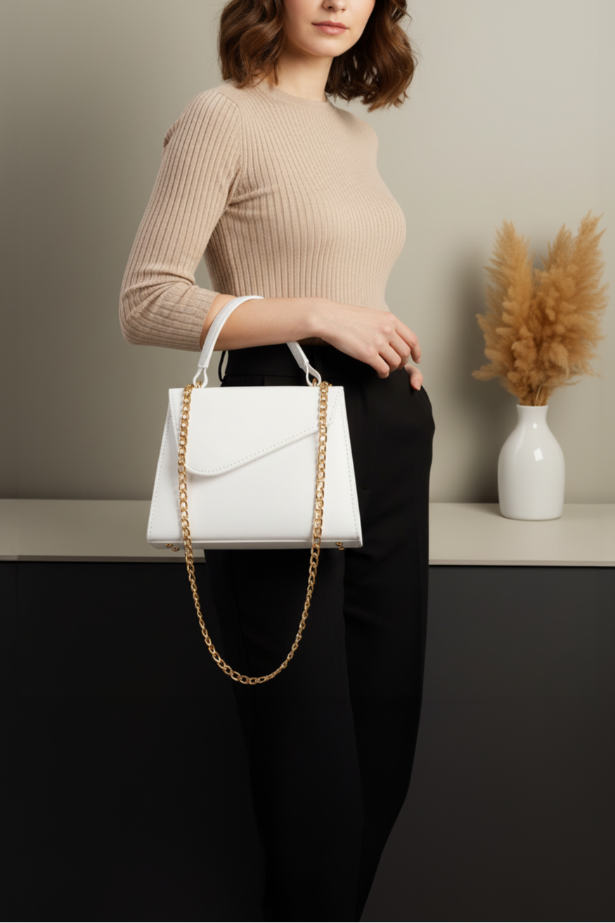 Woman holding a white handbag with a gold chain strap in a minimalistic setting.