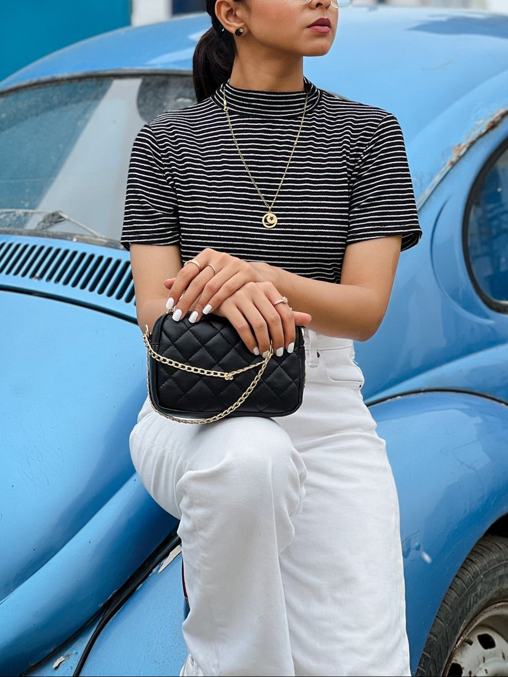 Woman holding a black Crossbody in front of a blue vintage car